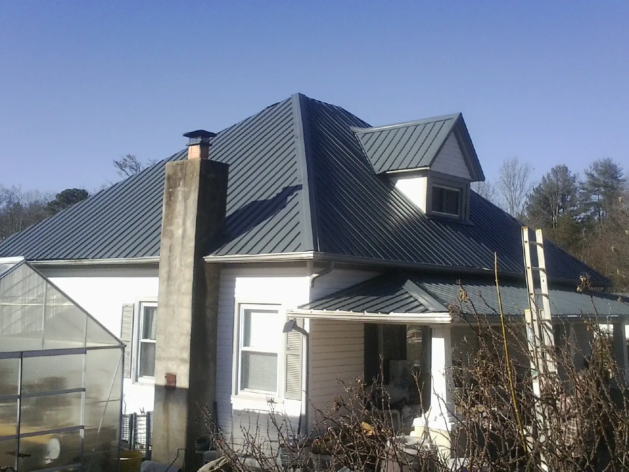 Dark blue standing seam metal roof on a white farmhouse with dormer — Slate & Tile Roof Repair by Roofing Brothers in Haskins
