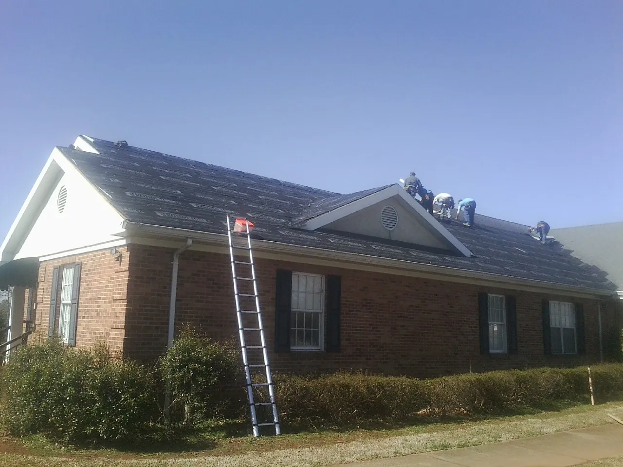 Crew tearing shingles off a brick ranch roof with a ladder set — Emergency Roof Repair work by our crew in Haskins
