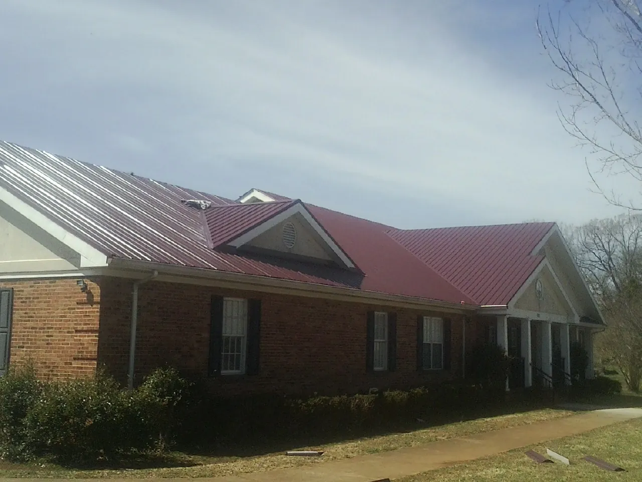 Red metal roof with gabled entries on a long brick building, from a Hail Damage Roof Repair job in Haskins