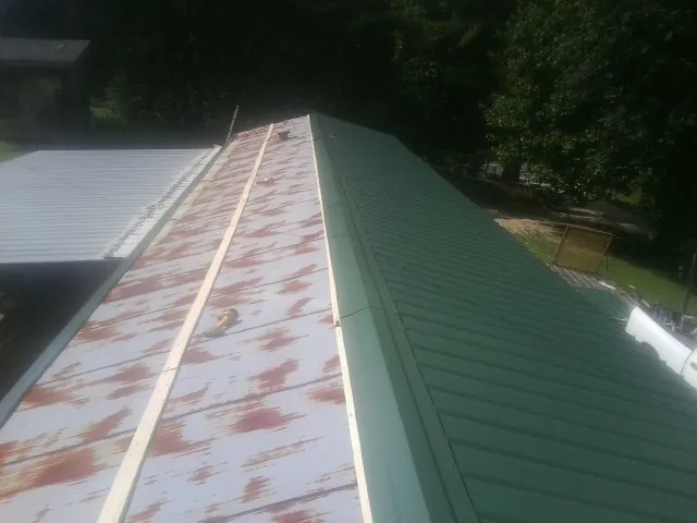 Old rusted panels beside newly installed green metal roofing — Wind Damage Roof Repair by Roofing Brothers in Haskins