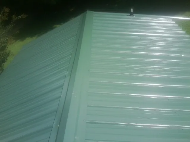 New green metal panels meeting at the ridge of a roof — Flat Roof Repair work by our crew in Haskins