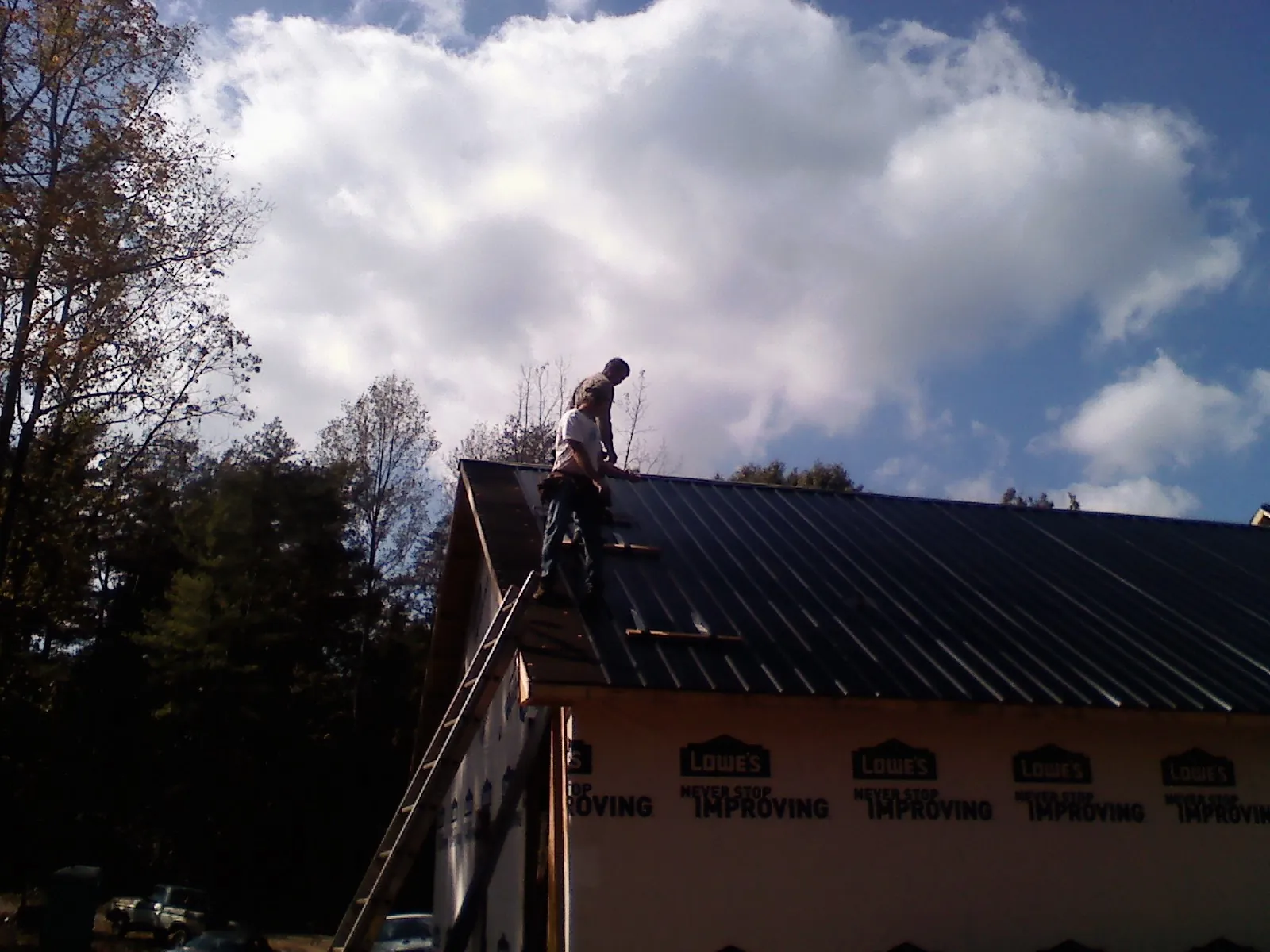 Roofer fastening dark metal panels high against a cloudy sky, from a Roof Inspection job in Haskins