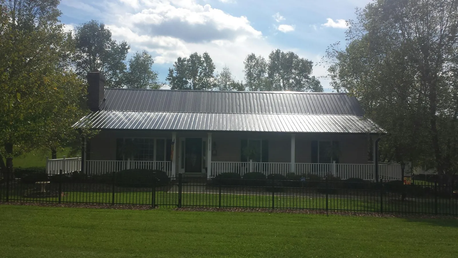 Gray metal roof on a brick ranch with a full width front porch — Gutter Guard Installation work by our crew in Haskins