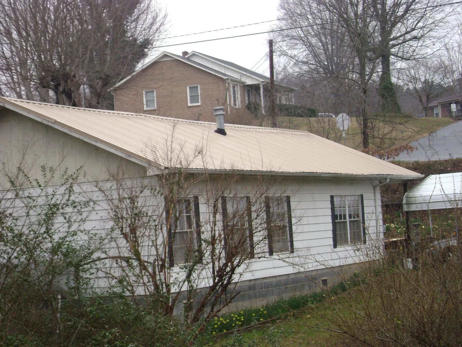 Tan metal roof on a white sided house set into a hillside — Commercial Roofing by Roofing Brothers in Haskins