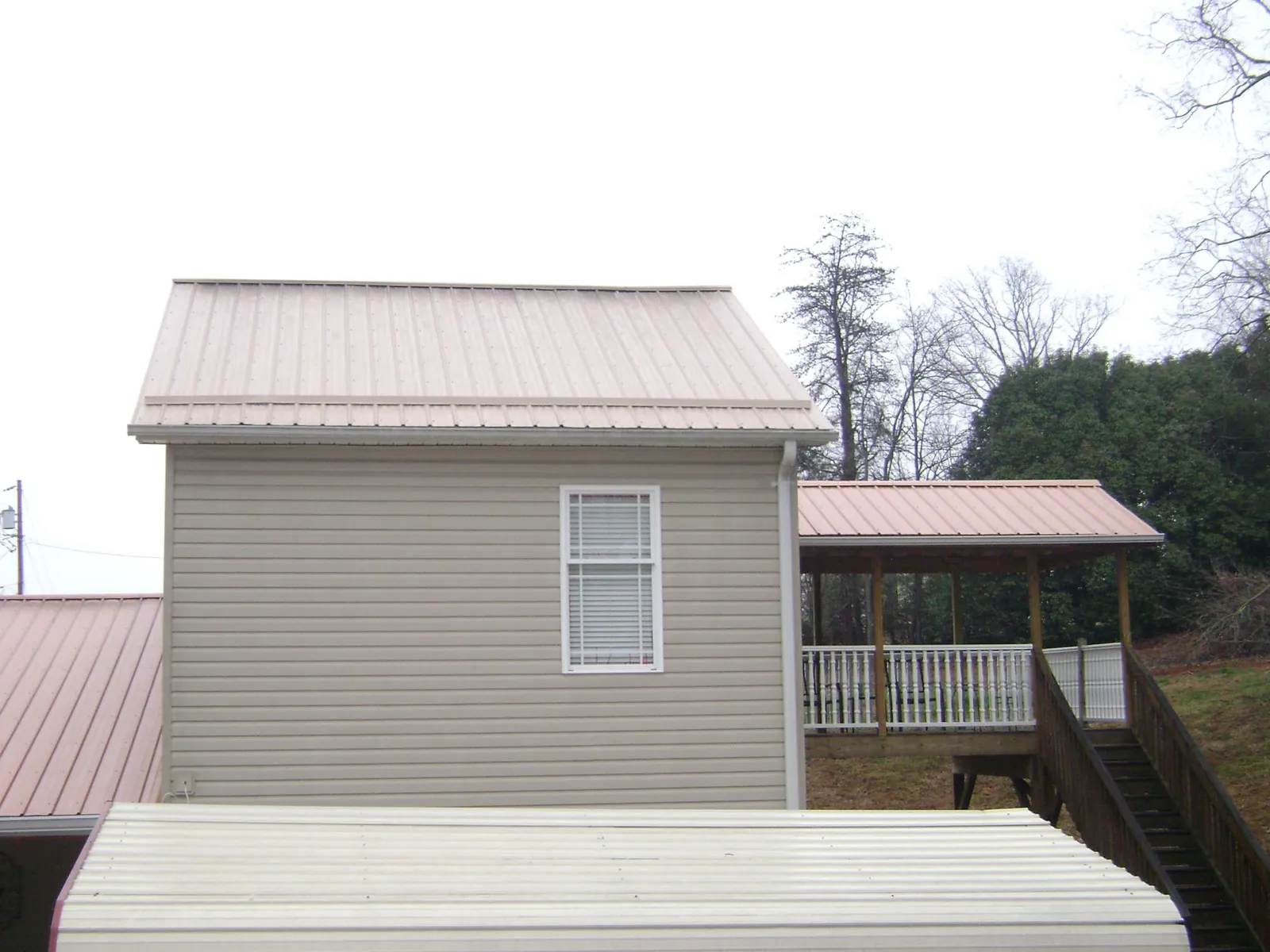 Tan metal roofs on a two story addition and attached porch, from a Roof Replacement job in Haskins